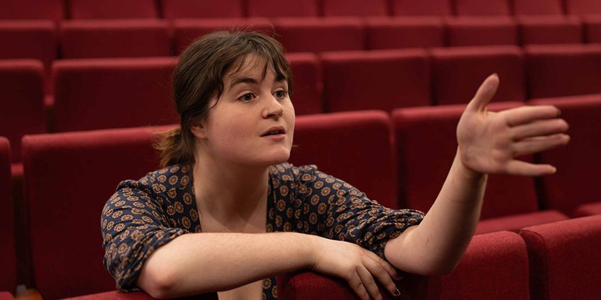 Maisie Johnson leaning forward in theatre seats talking to someone off camera