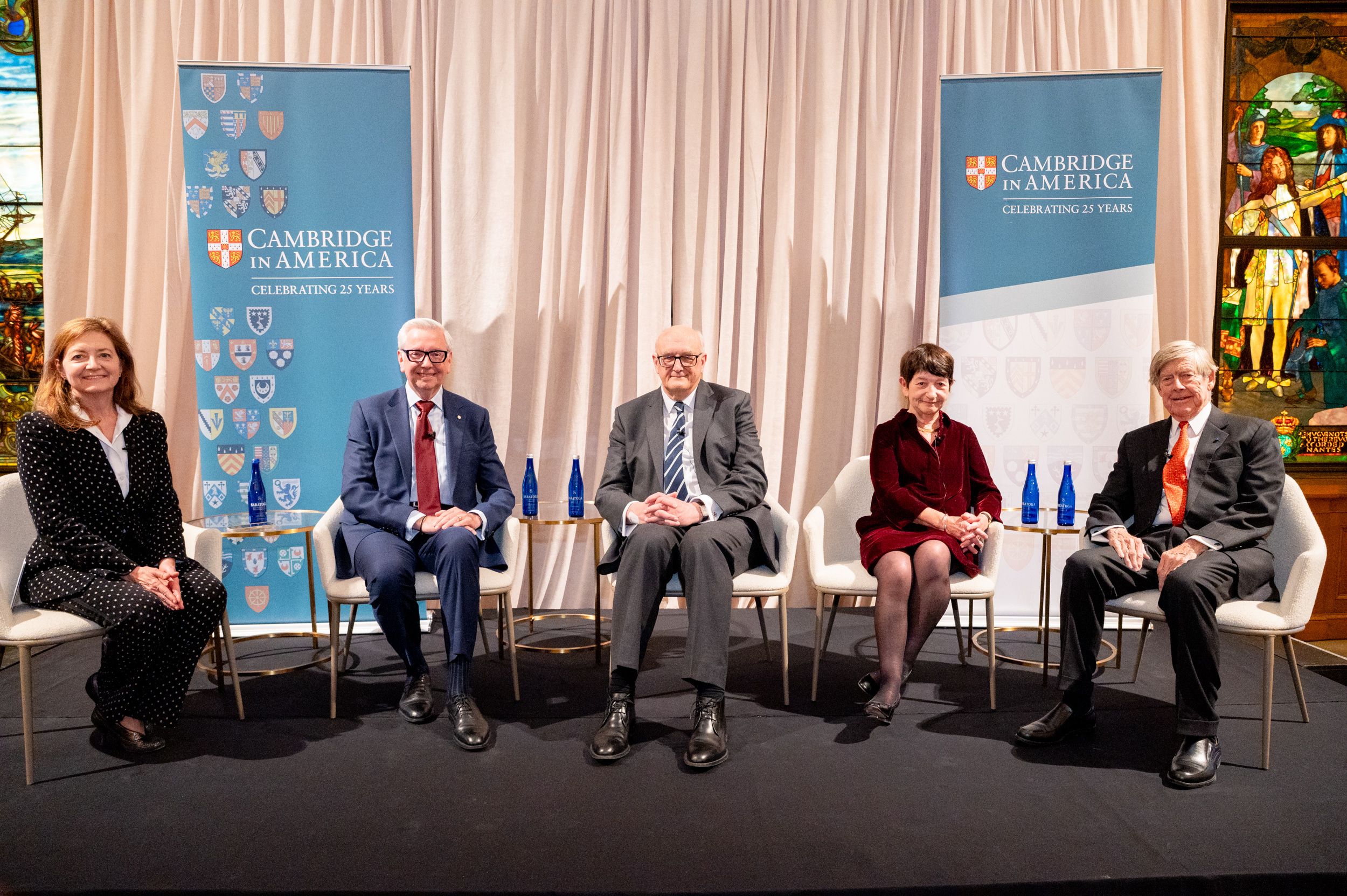 A panel of speakers on a stage with Cambridge in America banners