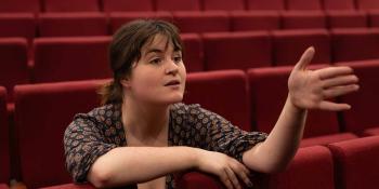 Maisie Johnson leaning forward in theatre seats talking to someone off camera