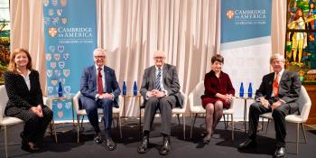 A panel of speakers on a stage with Cambridge in America banners