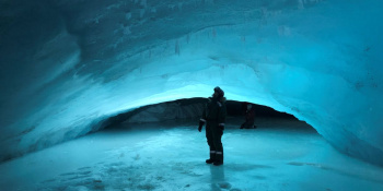 Person standing surrounded by ice under glacier