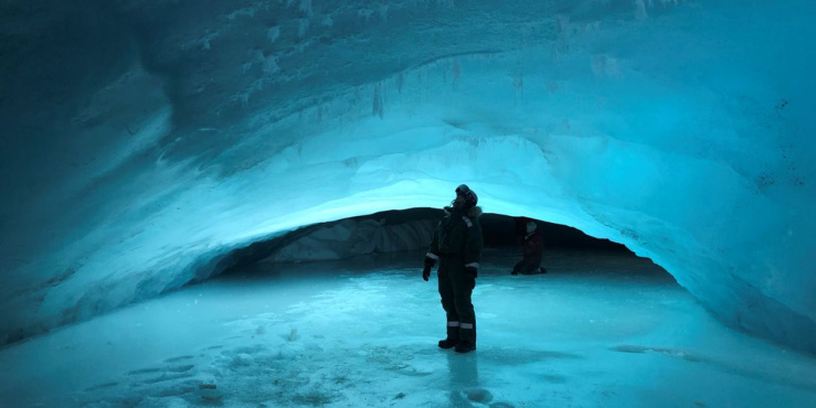 Person standing surrounded by ice under glacier