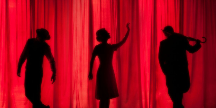 Three actors on a stage in front of a red curtain