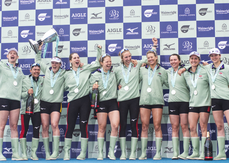 Wide shot of Cambridge rowing team celebrating with medals and a cup