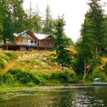 A cabin sits between trees fronting onto a lake