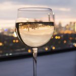 A glass of white wine sits in front of an evening City backdrop.
