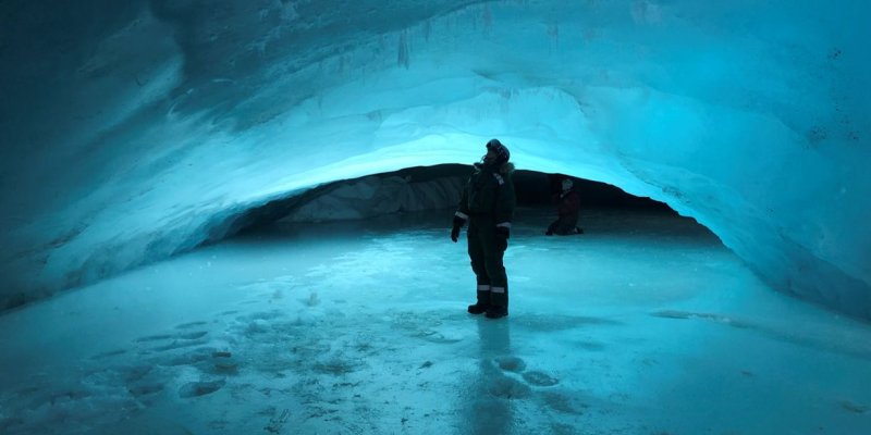 Person standing surrounded by ice under glacier