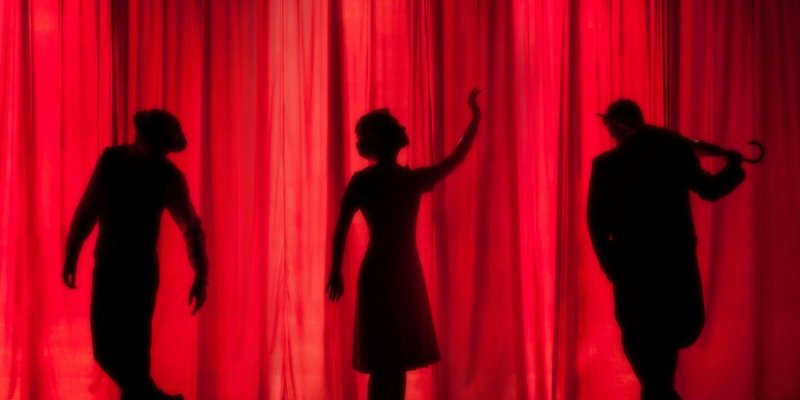 Three actors on a stage in front of a red curtain