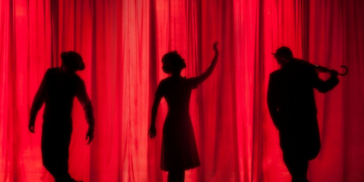 Three actors on a stage in front of a red curtain
